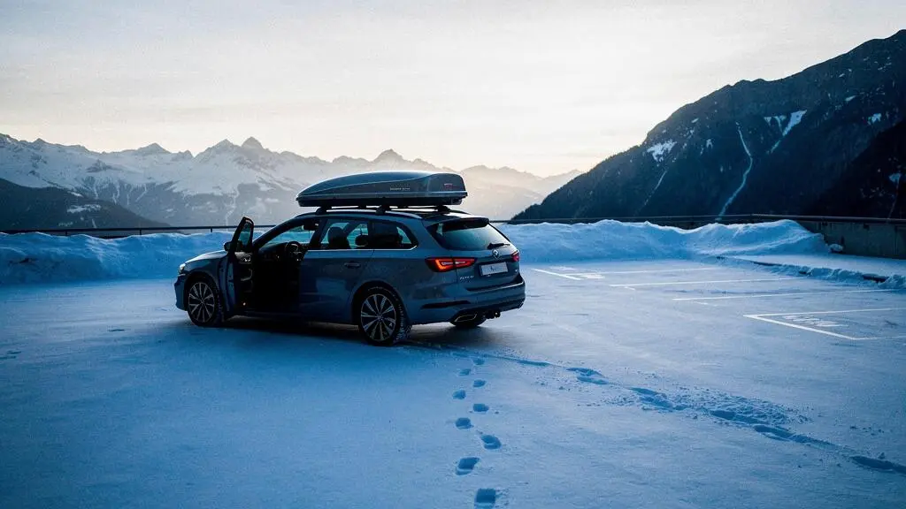 Coffre de toit fermé sur une voiture garée sur un parking de montagne enneigé, symbolisant le risque de cambriolage du matériel de ski