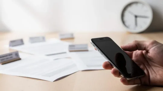 Main tenant un smartphone avec en arrière-plan des documents d'assurance flous symbolisant la comparaison rapide de plusieurs devis