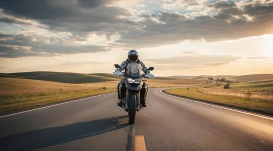 Motard équipé roulant seul sur une route ouverte au crépuscule, symbolisant la vulnérabilité et la nécessité d'une protection corporelle renforcée