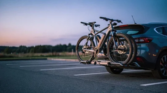 Deux vélos électriques fixés sur un porte-vélos à l'arrière d'une voiture, garés sur une aire de repos au crépuscule