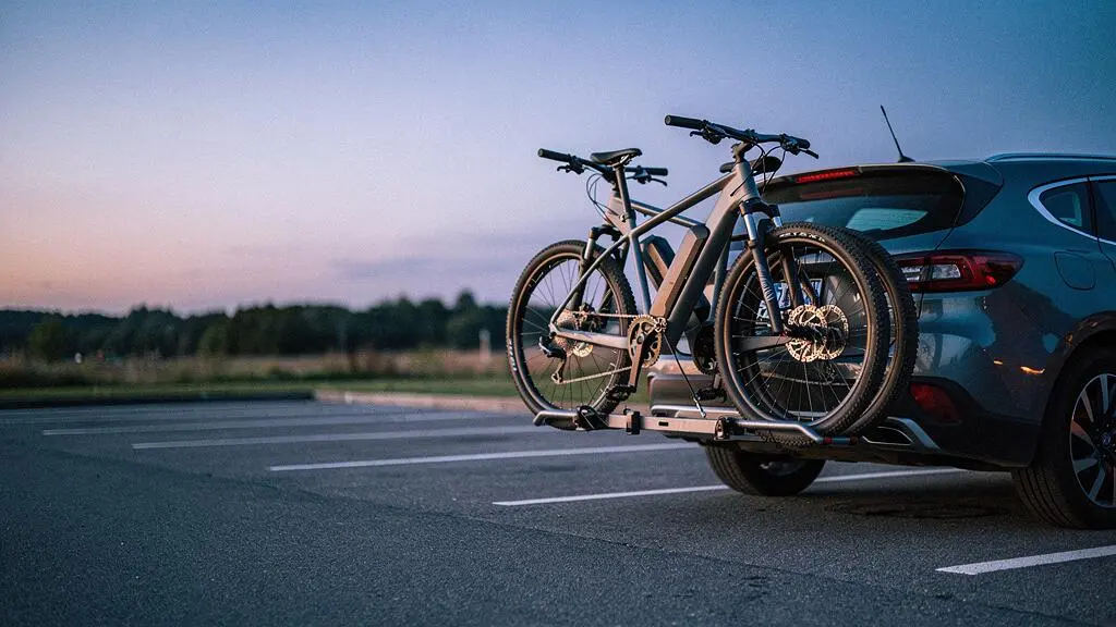 Deux vélos électriques fixés sur un porte-vélos à l'arrière d'une voiture, garés sur une aire de repos au crépuscule